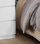 Gros plan d'une table de chevet ou d'une commode blanche à plusieurs tiroirs à côté d'un lit avec une literie grise et beige sur un plancher en bois
