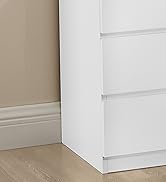 Gros plan d'un meuble à tiroirs blanc à trois tiroirs, au ras d'un mur beige. Plancher en bois clair et plinthe blanche visible en bas